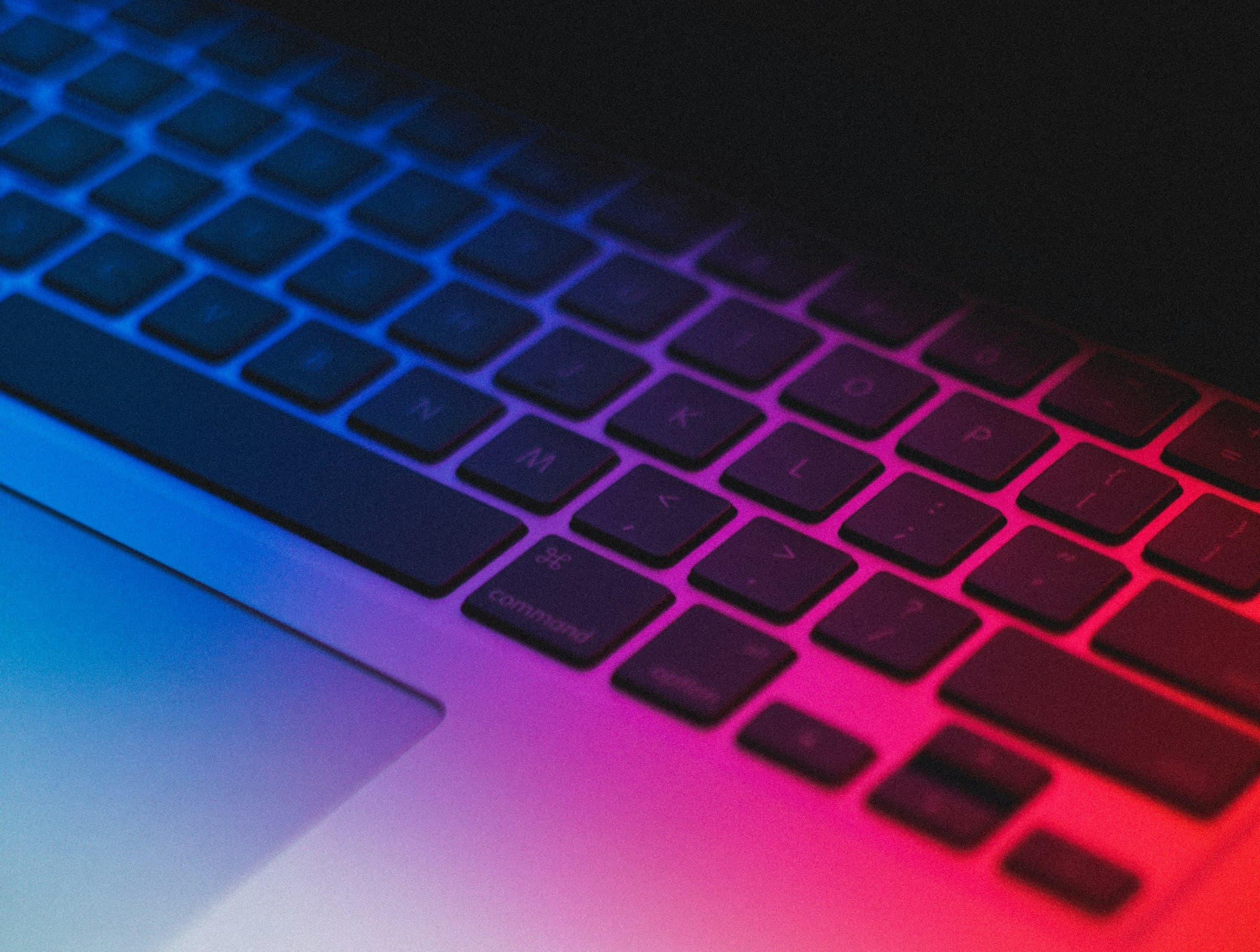 A close-up corner of a MacBook Pro keyboard lit in blue and red
