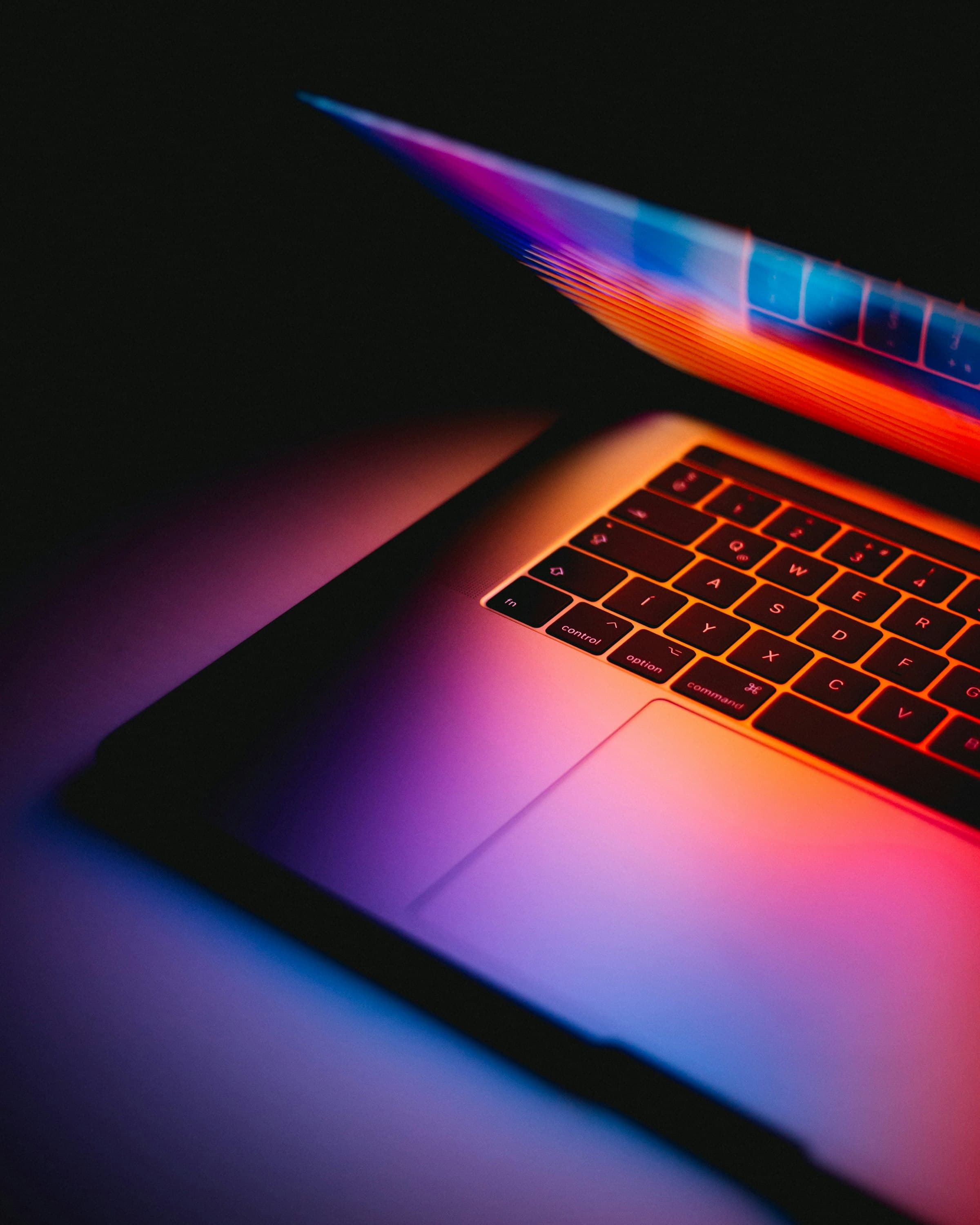 A MacBook Pro keyboard lit with dramatic rainbow light
